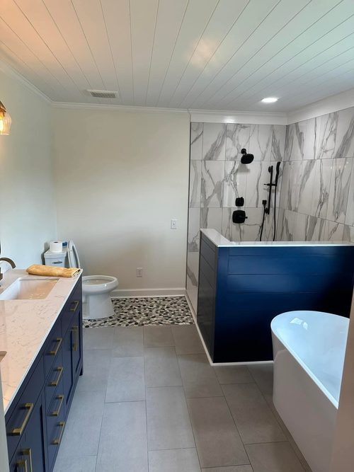 A finished bathroom with a navy vanity, a tiled shower and a freestanding tub.