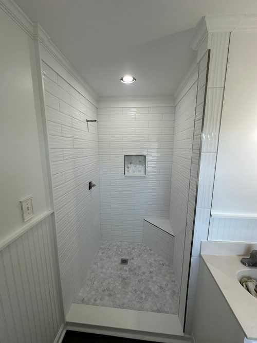 The rebuilt shower, tiled in white with a built in bench and a recessed shelf.