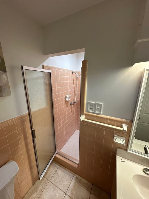 Dated bathroom with peach wall tile and a framed glass shower door.