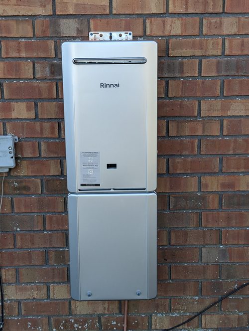 A Rinnai tankless water heater mounted and piped on an exterior brick wall.